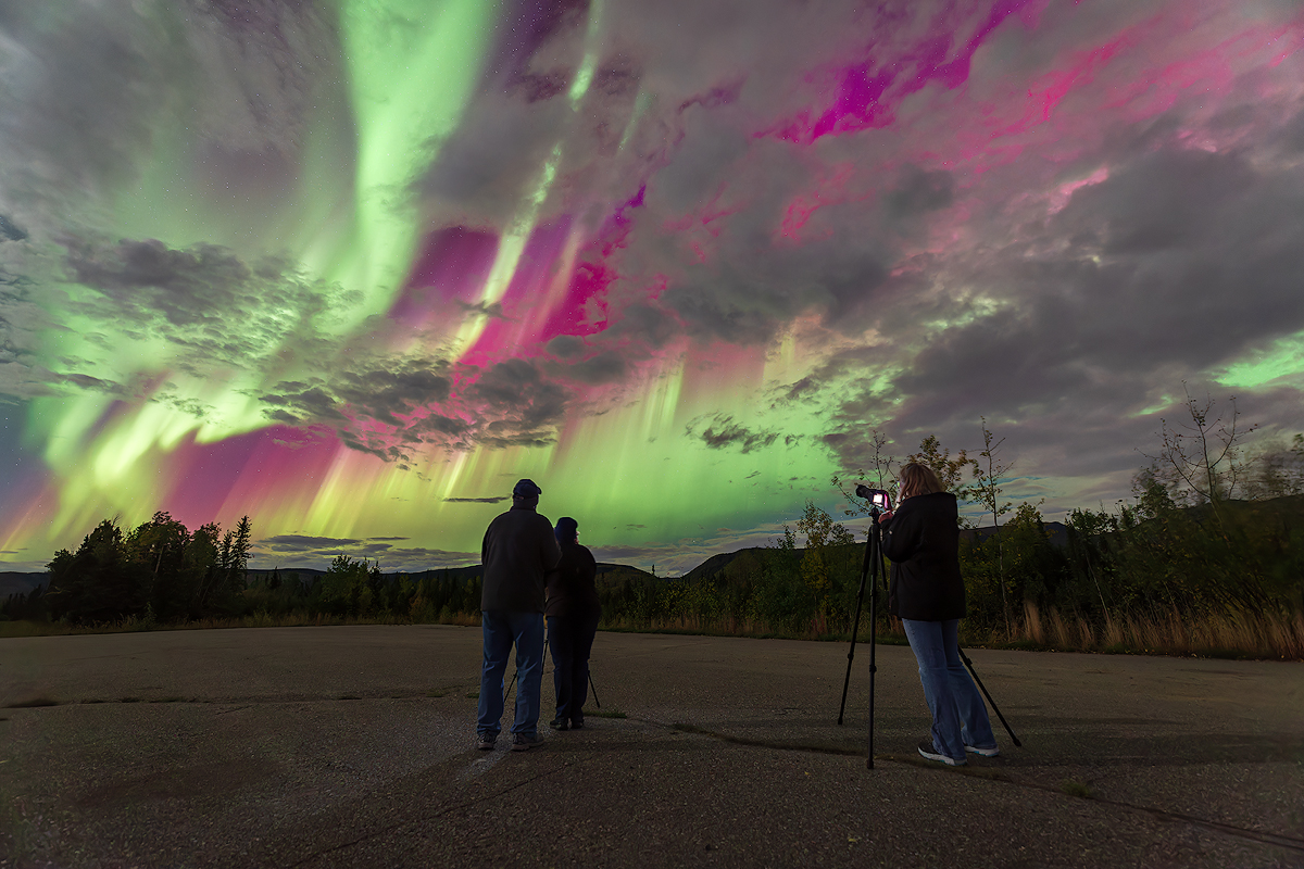 Couple viewing spectacular pink green and yellow aurora borealis from Alaska Highway during Face The Outdoors mobile aurora chasing tour near Fairbanks