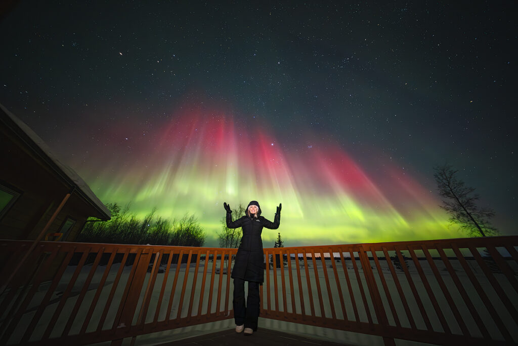 Excited guest celebrating spectacular pink and green northern lights aurora borealis from comfortable viewing deck at Face The Outdoors lodge Fairbanks Alaska