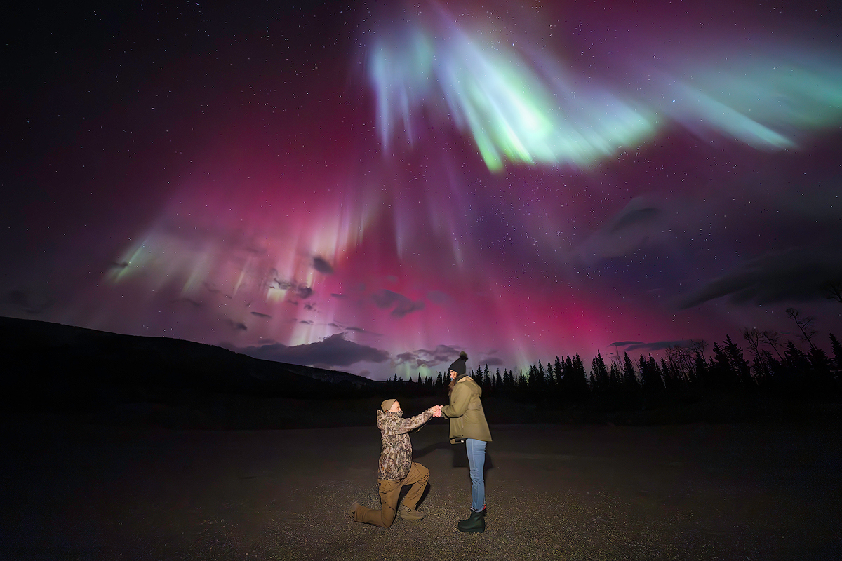 Romantic marriage proposal under dramatic pink and green northern lights aurora borealis with mountain silhouettes Face The Outdoors private tour Alaska