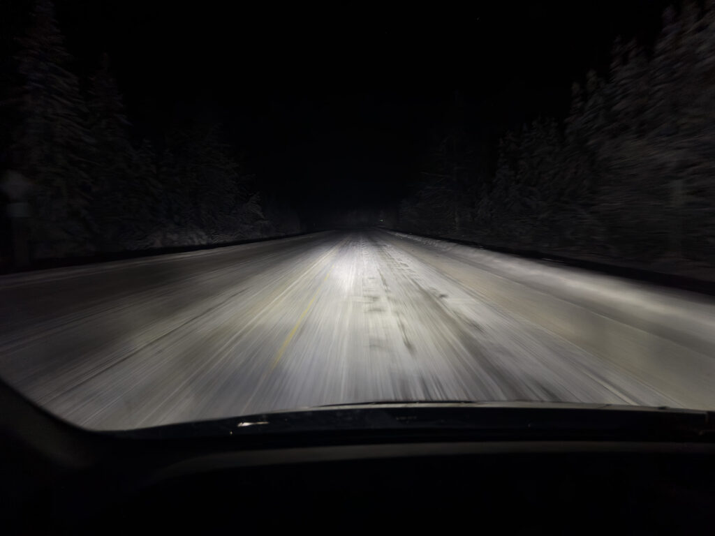 Dark icy Alaska winter road at night with limited visibility showing challenging driving conditions for aurora chasers