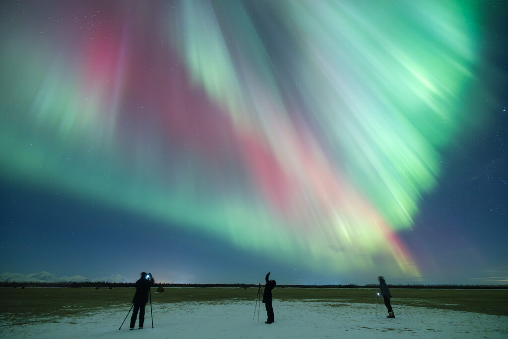 Excited tourists viewing spectacular northern lights display with experienced guide pointing out aurora features and explaining the phenomenon