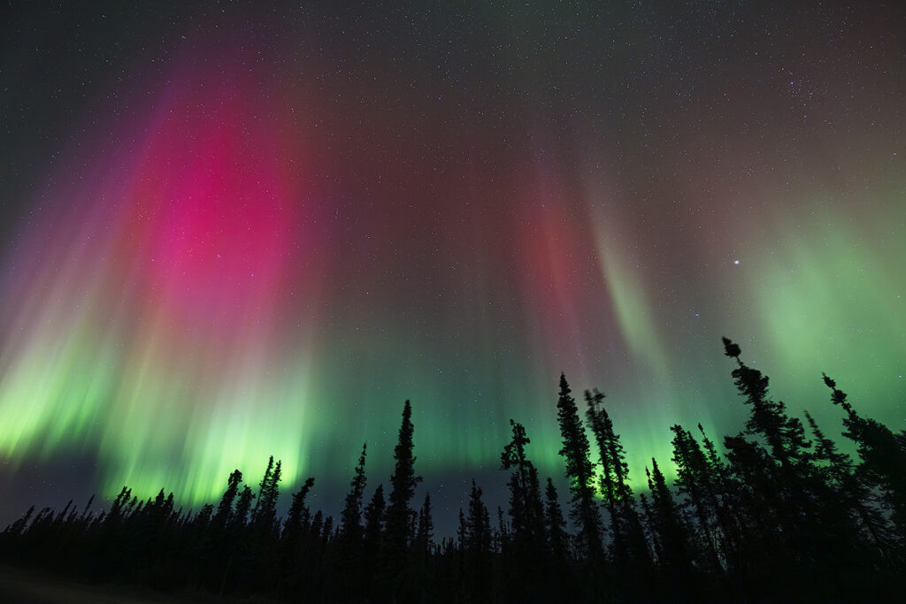 Aurora borealis over Fairbanks showing green and red color bands produced by charged particles striking oxygen and nitrogen in Earth's atmosphere