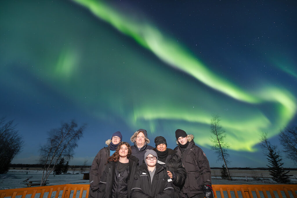 Fairbanks aurora guide leading a small group northern lights tour at Face The Outdoors lodge with aurora visible overhead
