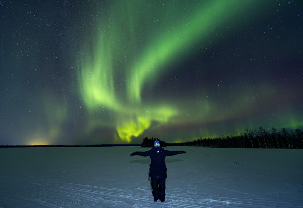What to pack aurora Alaska – properly dressed viewer with balaclava, mittens, and full winter gear enjoying northern lights in Fairbanks