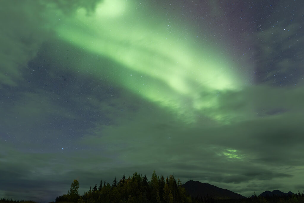 Northern lights visible through cloud gaps in Fairbanks Alaska showing why cloud cover monitoring and mobile chasing matter for aurora tours