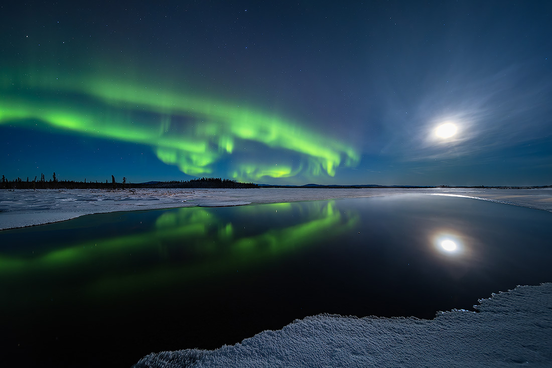 Northern lights and moon reflected in open water under a clear dark Alaska sky