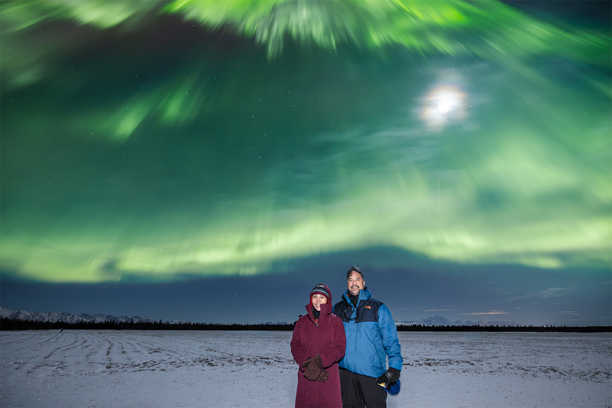 Face The Outdoors tour guests under green aurora and a full moon near Fairbanks