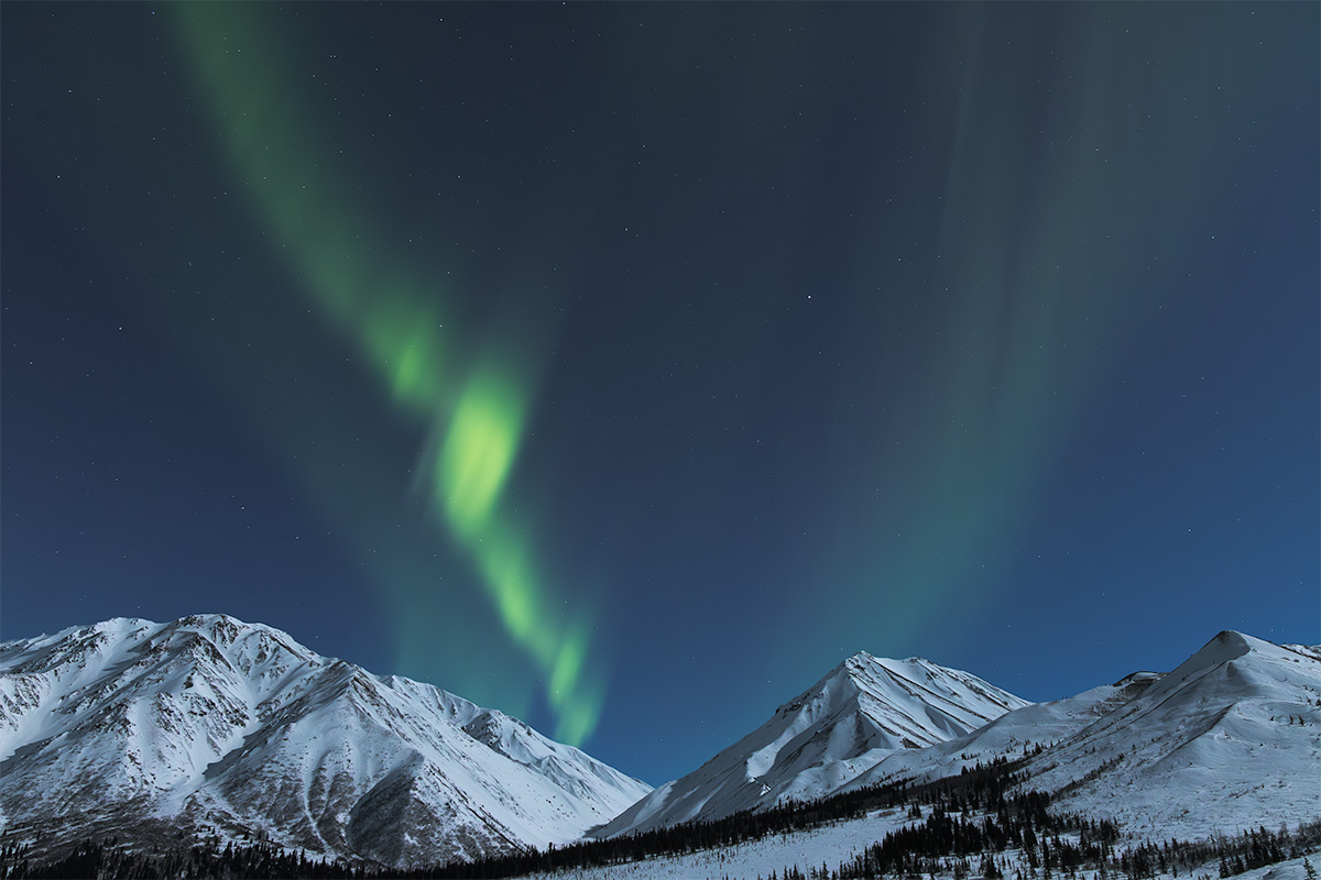 Soft blue-green aurora over snow-covered mountains showing how a faint display looks to the eye